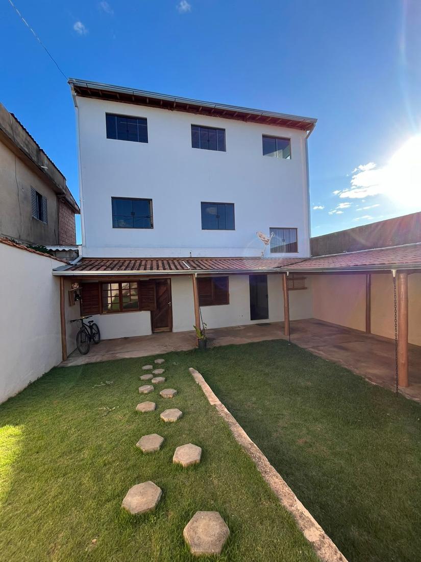Fachada da casa de três pavimentos vista do quintal gramado, com garagem coberta ao lado