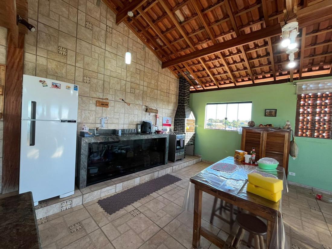 Área gourmet com bancada de granito, fogão, churrasqueira de tijolinho e mesa de madeira